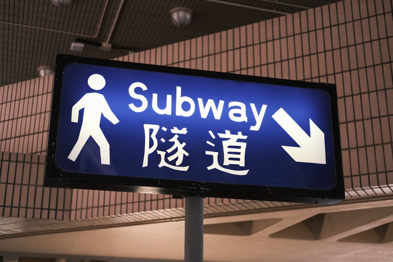 Blue subway entrance sign in Kowloon, Hong Kong with directional arrow.