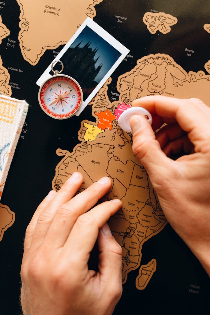 about-img Close-up of hands scratching a travel map, featuring a compass and polaroid, symbolizing travel planning.