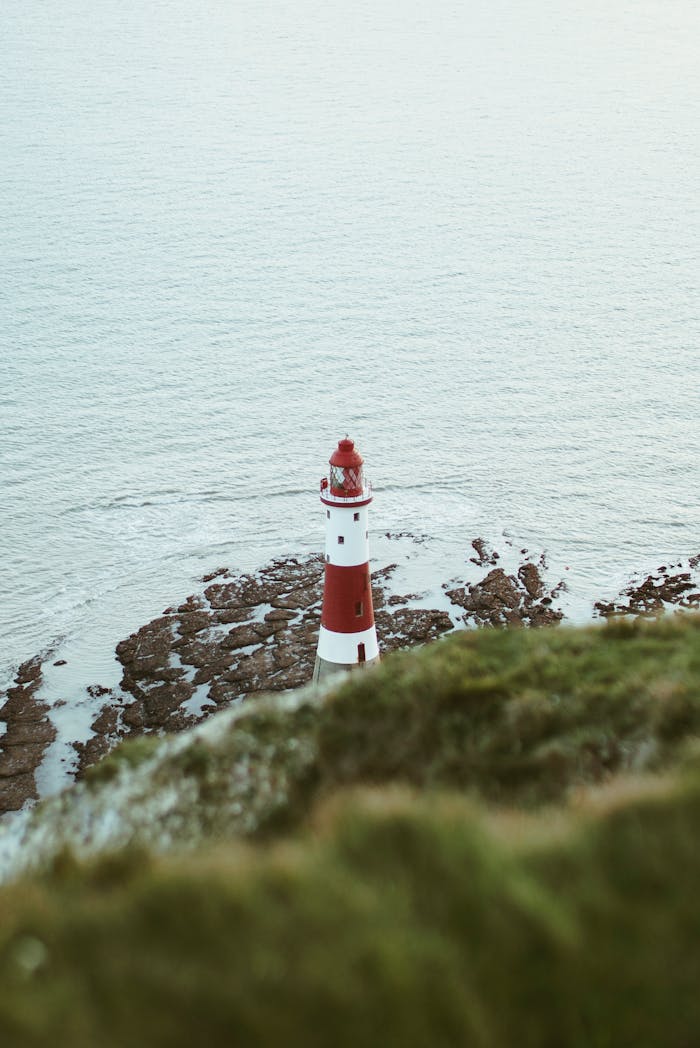 services-03 Aerial view of a red and white lighthouse on a rocky seashore surrounded by calm ocean waves.
